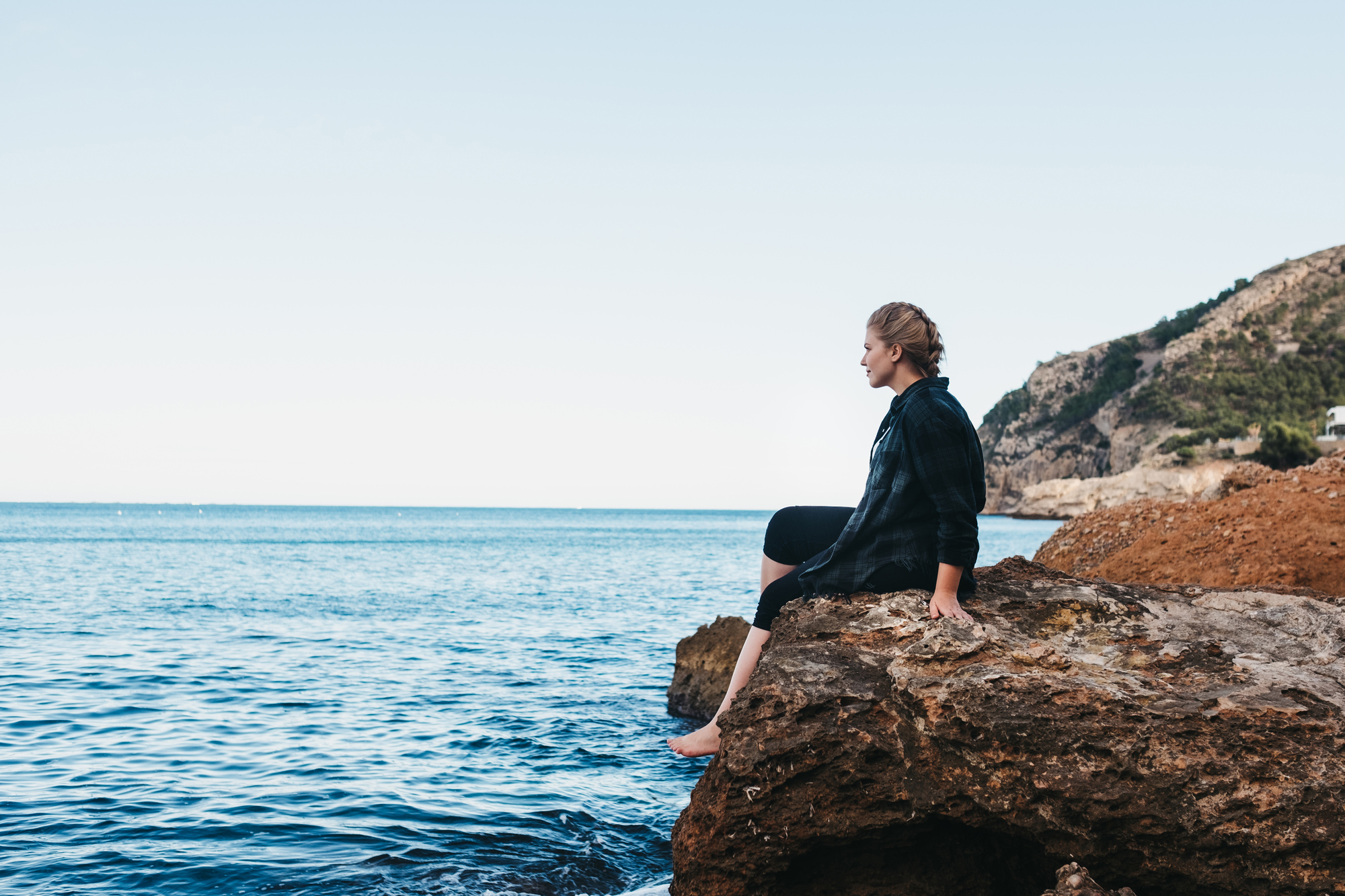 Nainen istuu kalliolla meren äärellä