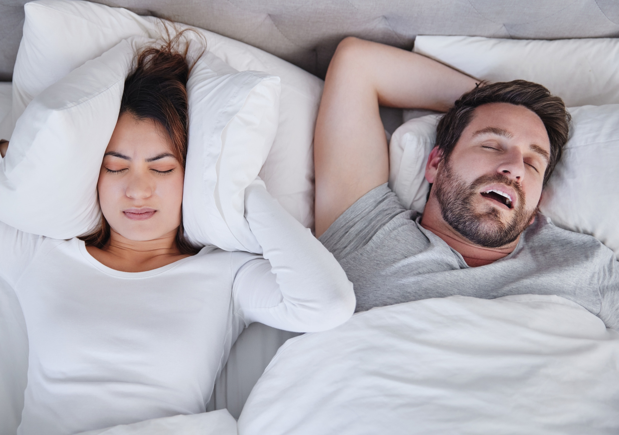 A person snoring and another one holding their ears