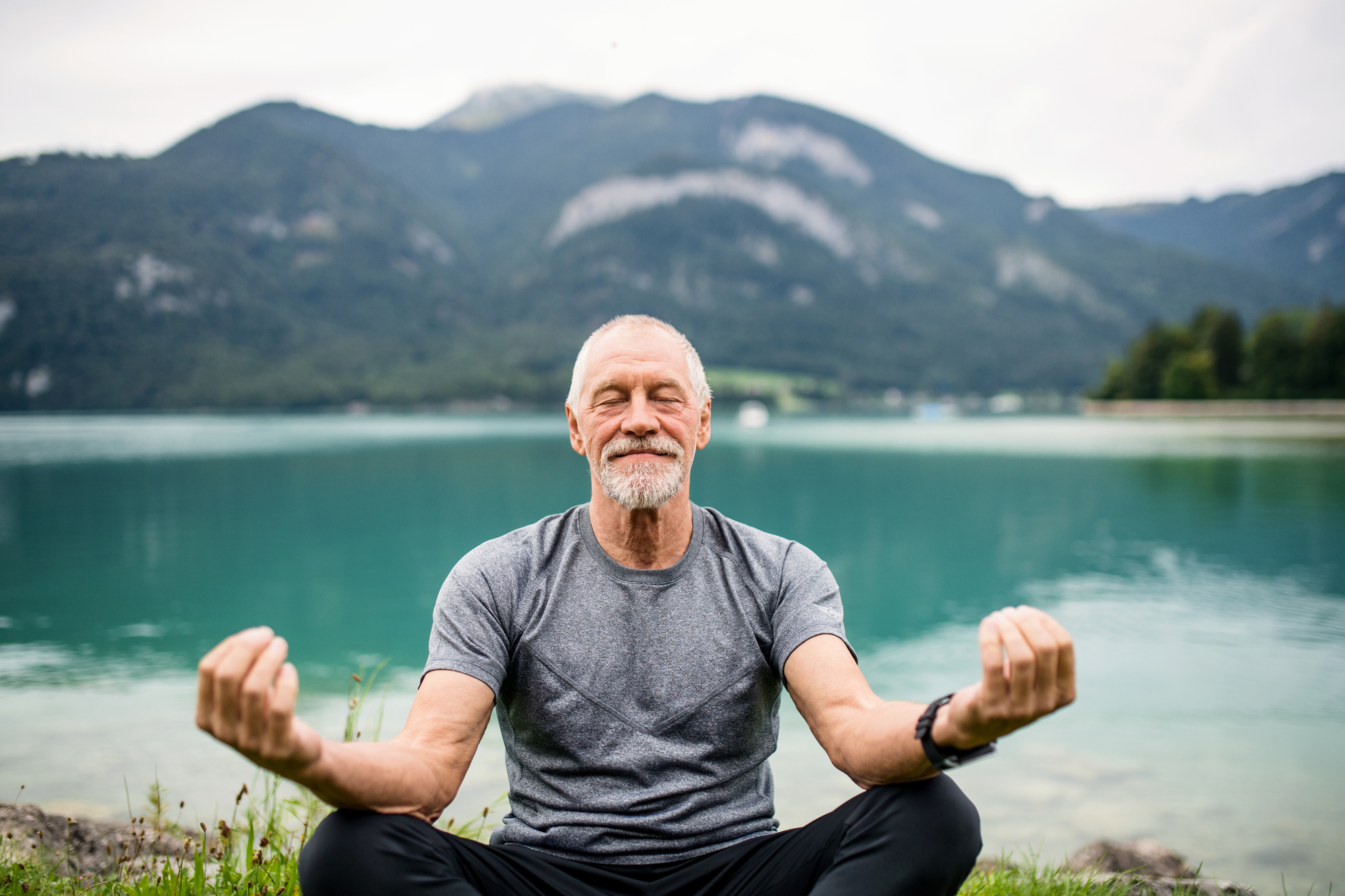 A senior man practizing mediation at a lake